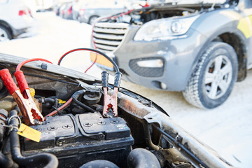 Charging automobile discharged battery by booster jumper cables at winter