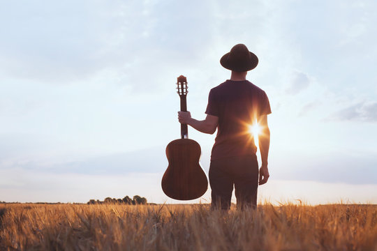 music festival background, silhouette of musician artist with acoustic guitar at sunset field.