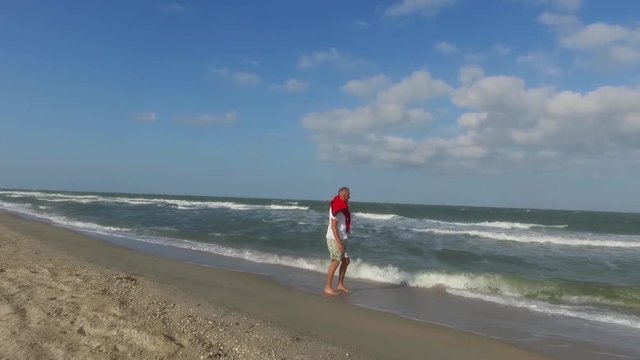 Joyful man walking along the surf line at sunny windy day. Slow motion