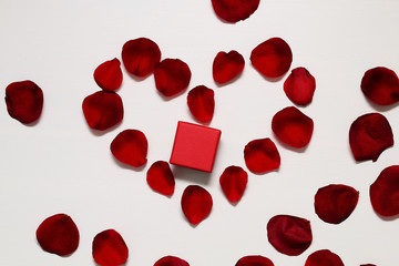 Red gift box on a bright red rose petals on a white background Valentine's Day.