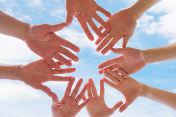 team or brotherhood concept, group of people putting hands together against blue sky