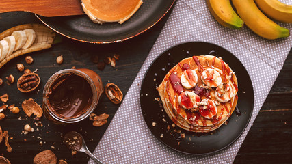 Pancake with chocolate and nut paste, walnuts and banana on a black plate