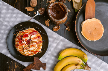 Pancake with chocolate and nut paste, walnuts and banana on a black plate