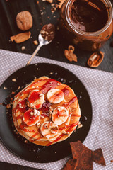 Pancake with chocolate and nut paste, walnuts and banana on a black plate