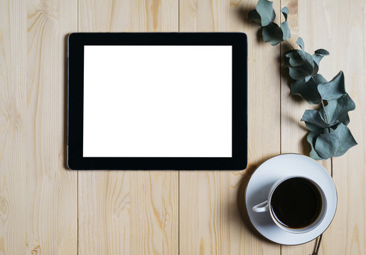 Tablet with a clean blank screen mockup monitor with a branch of eucalyptus and a cup of coffee on a wooden background with natural wood planks top view vertical, mock up concept, computer technology