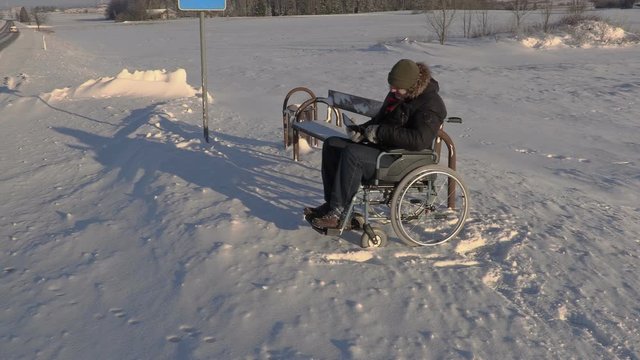 Disabled man on wheelchair talking using tablet near bus stop