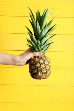 Female hand holding ripe pineapple on a yellow wooden background