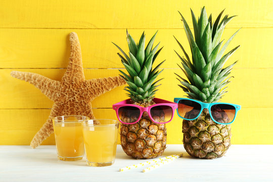Ripe pineapples with glasses of juice on a white wooden table