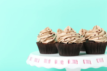 Tasty cupcakes on cake stand on green background
