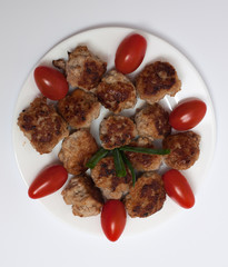 fried meatballs, with plum tomatoes, on a white plate, on a light background