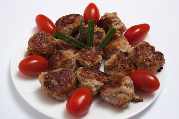 fried meatballs, with plum tomatoes, on a white plate, on a light background