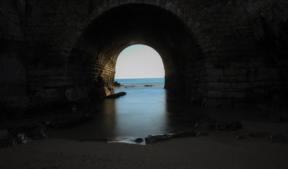Fototapeta na wymiar Big stone wall with a tunnel to the sea