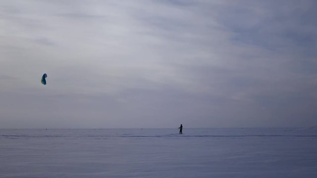 a young man learns to control a parachute from the kiteboarding while standing on a frozen lake in winter, 4k