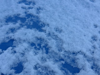 Schnee und Eis  auf einem gefrorenen Fensterglas vor blauem Himmel