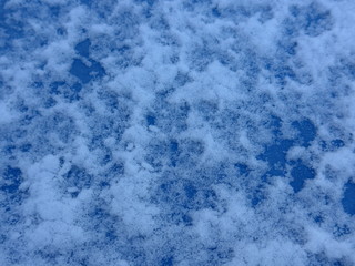 Schnee und Eis  auf einem gefrorenen Fensterglas vor blauem Himmel