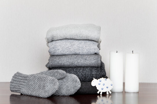 Pile of grey knitted sweaters and mittens on wooden table, decorated with candles