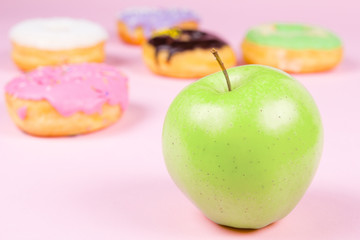 Close-up of tasty donuts and fresh green apple on pink background suggesting healthy food concept
