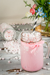 Pink hot chocolate with marshmallow, - with flowers and jar with marshmallows in the background. Spring mood. On an old white wooden table.