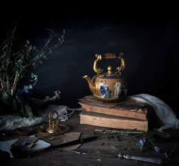 still life. vintage gold with enamel kettle, books and clock on the wooden table. dark background. space for text