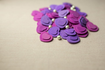 Obraz na płótnie Canvas Purple hearts and pearls lying on a beige fabric