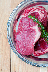 Two raw ribeye steak with rosemary and olive oil.