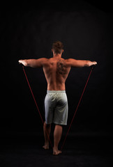 Fototapeta premium rear view on strong man with heavy body making exercises with expander on black background.