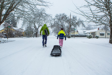 Children walk down the center of an empty street dragging sleds in the freshly fallen winter snow.