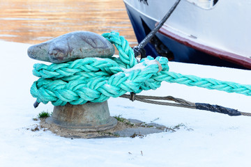Bound boat moored on the waterfront in winter. Prague snowy embankment. Moorings on the River Vltava. Green rope tied to an anchor stake.  © karelpesorna