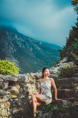 Naklejka premium Feminine romantic woman posing in Stari Bar old fortress, Montenegro. Tanned female with long hair, red lips and manicure in white dress flowers. Brunette girl walk around oldest castle