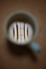 Fluorescent tube reflection in a white cup of tea on brown table. Top view