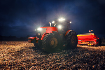 Naklejka premium Tractor preparing land with seedbed cultivator at night