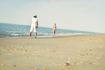 Happy couple walking on beach, male talking using mobile phone. Natural outdoors background. Back view