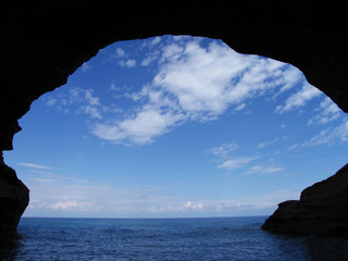Blue sky with white clouds over the sea and black cave silhouette