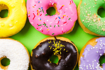 Colorful round donuts on green background. Flat lay, top view.