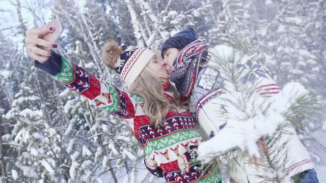 Romantic couple in snowy forest kissing and taking selfie