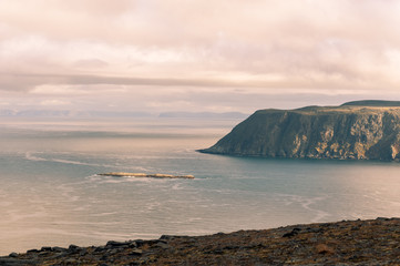 Rocky coast with big cliffs falling into a calm sea at sunset