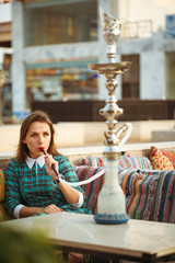 Beautiful young woman smokes a hookah in a cafe