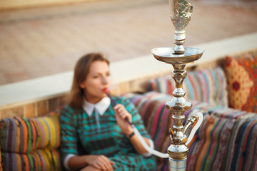 Beautiful young woman smokes a hookah in a cafe