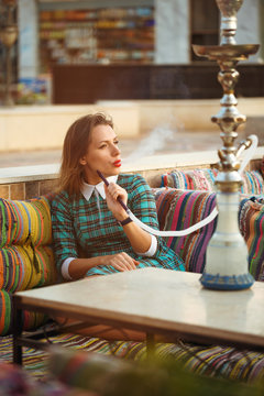 Beautiful young woman smokes a hookah in a cafe