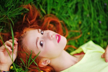Obraz na płótnie Canvas beautiful red-haired girl in a yellow shirt lying on the grass and stares dreamily