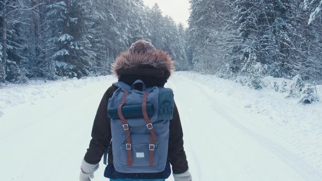 RL PAN Young female hiking with a backpack in beautiful winter forest, walking on a road away from the camera, light snowfall. 4K UHD, 60 FPS SLO MO, RAW edited footage