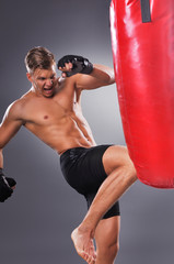 Muscular Fighter Practicing Some Kicks with Punching Bag. Boxing on the Gray Background. Concept of Healthy Lifestyle.