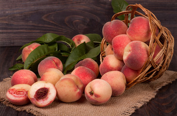 peaches in a wicker basket with leaves on wooden table