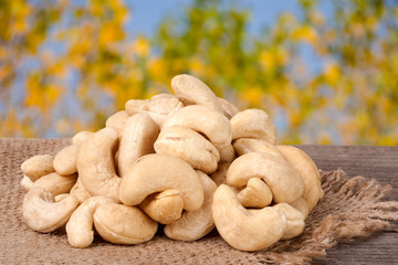 heap of cashew nuts on a wooden table with sacking and blurred garden background