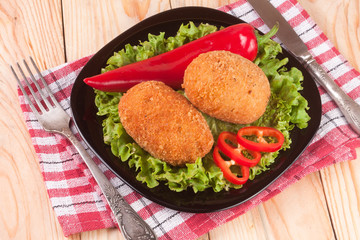 two fried breaded cutlet with lettuce on a black plate and wooden background