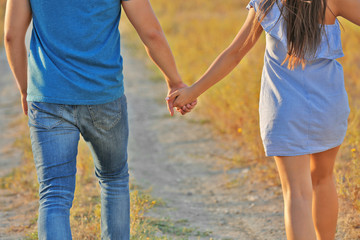 Young couple in love with holding hands walking on meadow on sunset