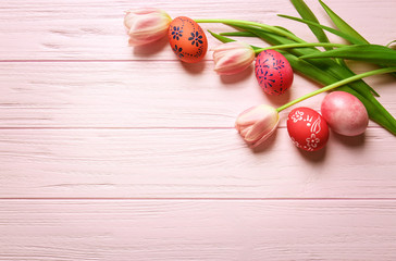Colourful Easter eggs with floral ornament and fresh tulips on pink wooden background
