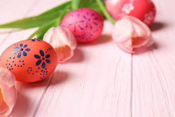 Fototapeta na wymiar Colourful Easter eggs with floral ornament and fresh tulips on pink wooden background, closeup