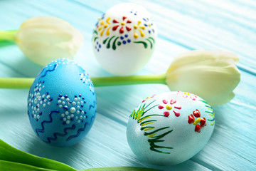 Beautiful Easter composition with decorated eggs and flowers on blue wooden background, closeup