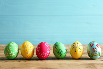 Fototapeta na wymiar Colourful Easter eggs with floral ornament in a row on wooden table and blue background, closeup
